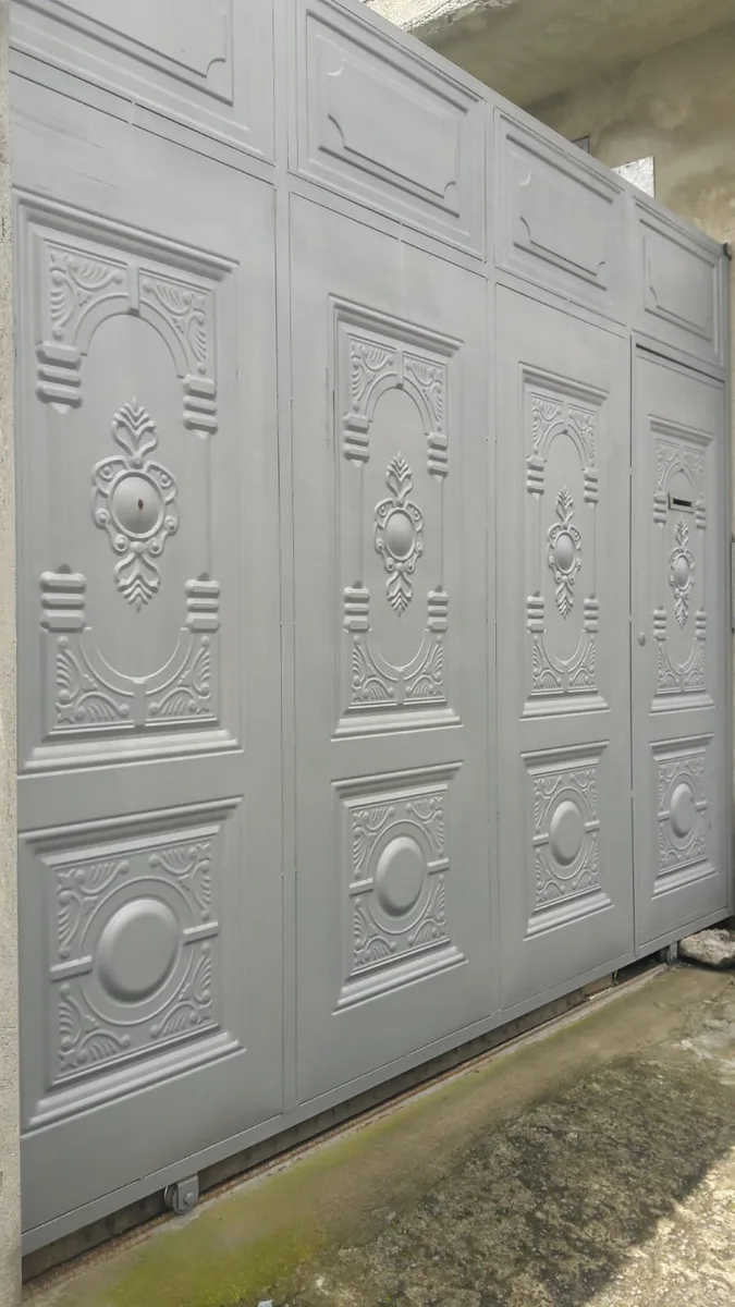 Portón metálico gris con tableros decorativos en Quito