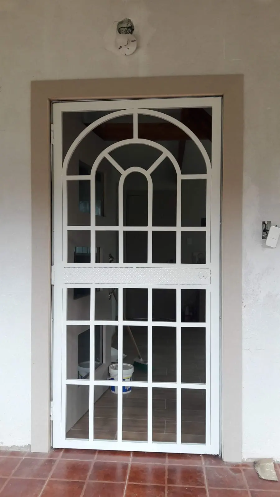 Cubre-puerta blanco con cuadrícula y arco superior sobre puerta de vidrio