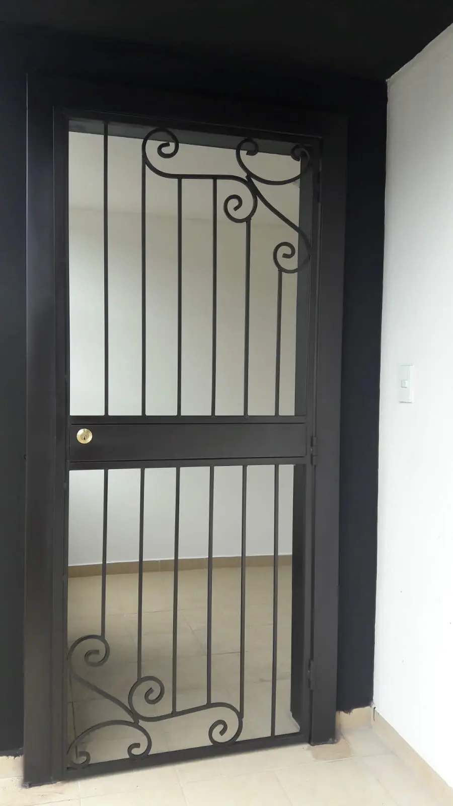 Cubre-puerta de hierro negro con barrotes verticales y volutas