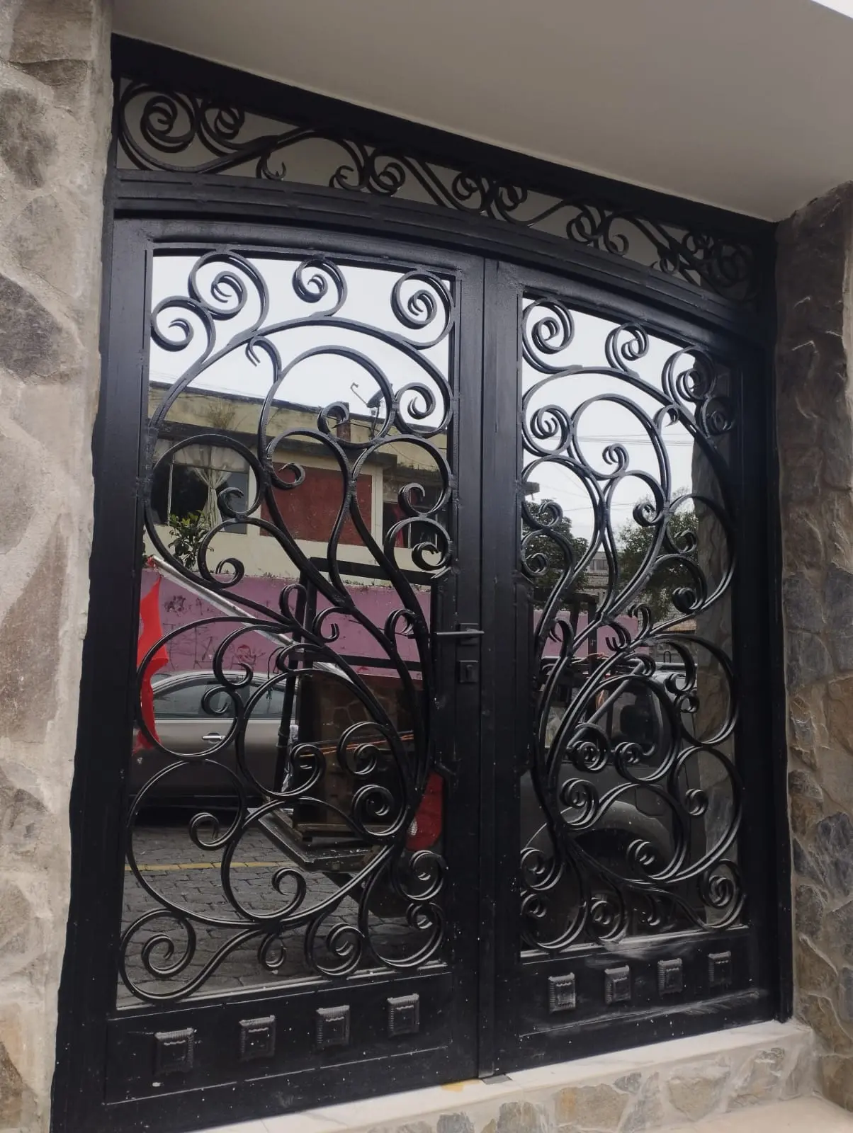 Puerta doble de hierro forjado negra con arco superior y volutas