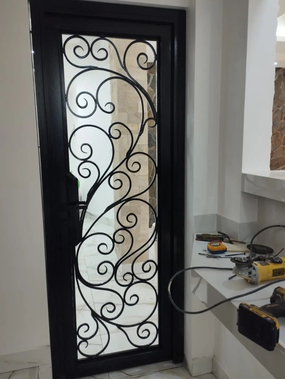 Puerta de hierro forjado negra con volutas ornamentales y vidrio