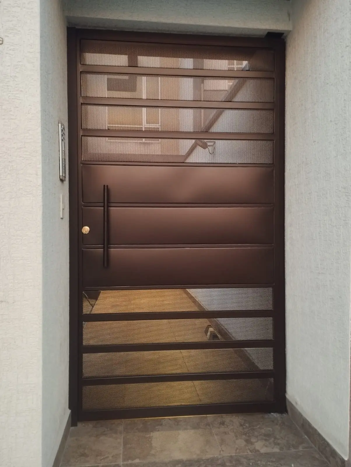 Puerta metálica de tool perforado color café con manillón vertical, fabricada en Quito