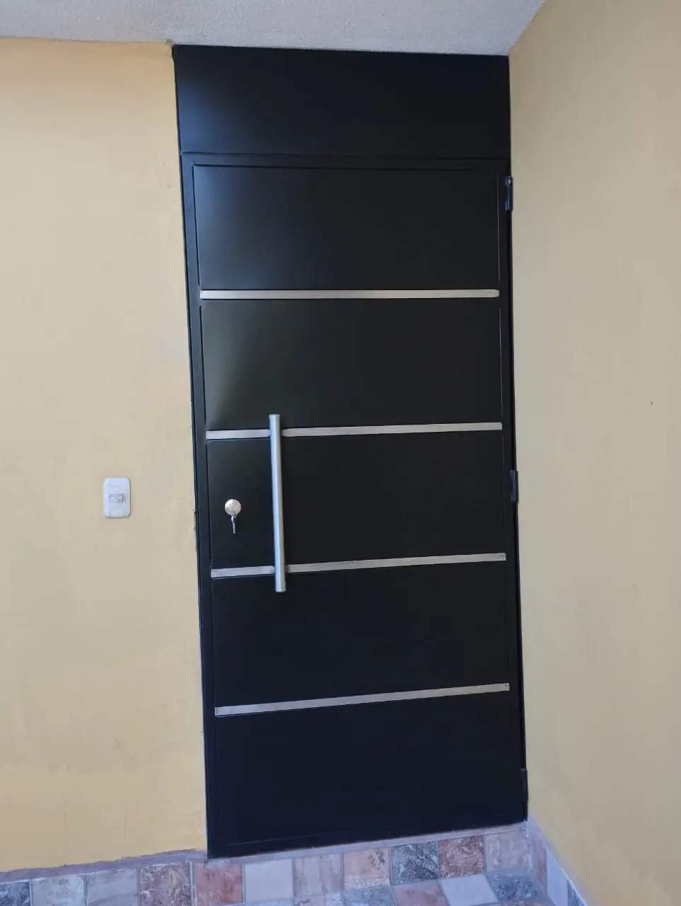 Puerta tamborada negra con franjas plateadas y manillón vertical