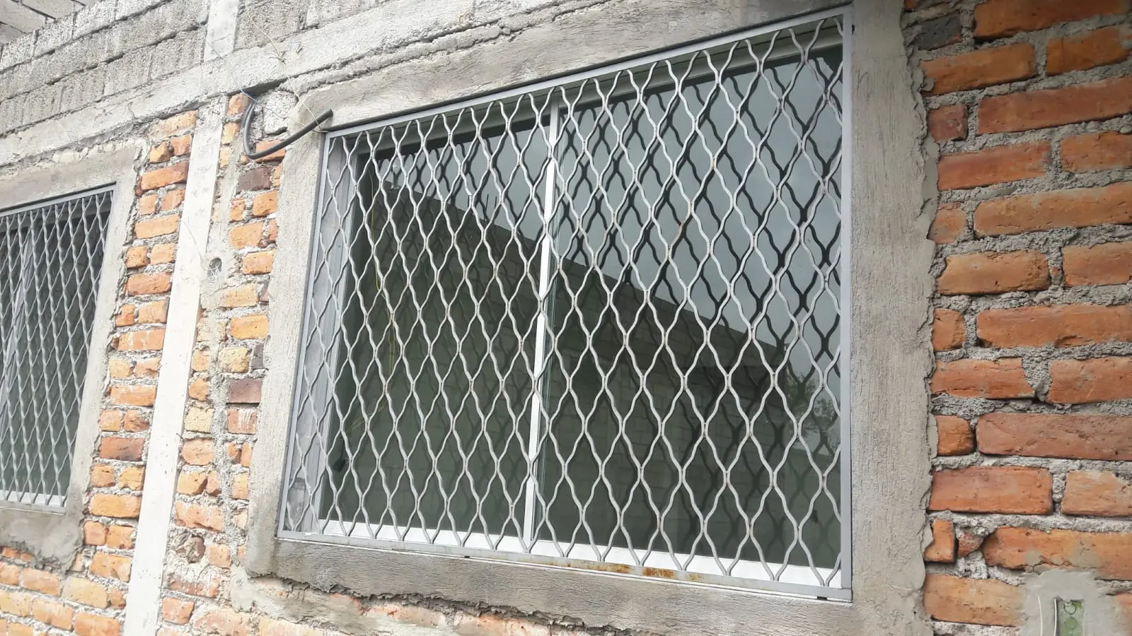 Cubre-ventana blanco de rombos sobre fachada de ladrillo